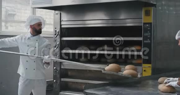 商业烘焙行业有魅力的面包师和他的专业协助从烤箱机上取出熟面包视频的预览图