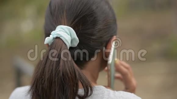 在自然公园里一位戴着眼镜的亚洲女人在手机上交谈她从后侧近距离拍摄视频的预览图