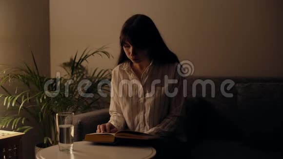 集中精力的年轻女子正在黑暗的房间里看书台灯发出的光视频的预览图