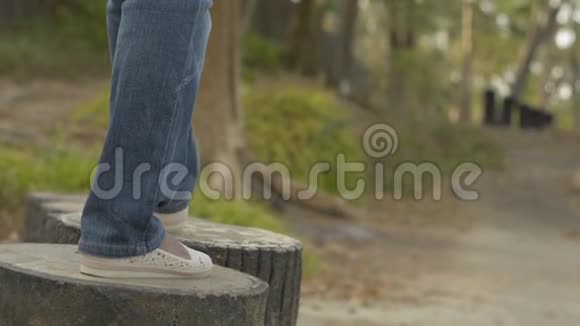 随着镜头从后面的女人腿穿牛仔裤悠闲地走在混凝土树桩在自然公园夏天视频的预览图