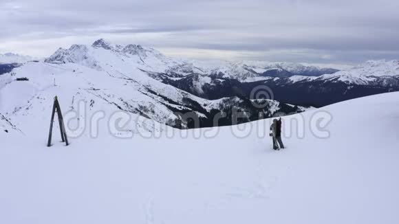 徒步旅行者带着背包和滑雪板站在雪山山顶上从上面可以看到风景视频的预览图