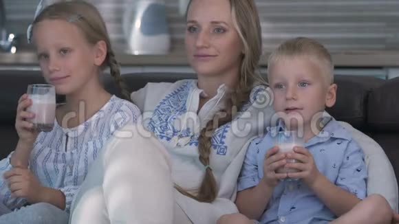 妈妈和两个孩子坐在沙发上看电视孩子们喝可可视频的预览图