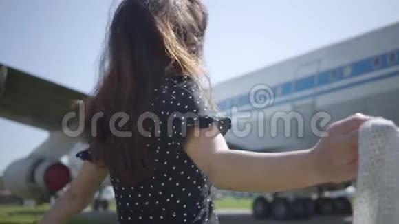 在大飞机前披着白色披肩的年轻黑发女孩的后景夏天旅行的快乐视频的预览图