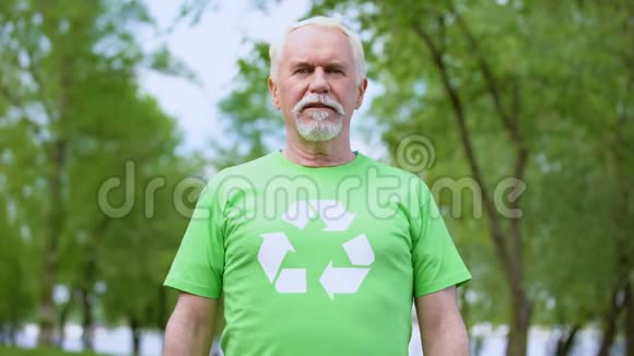 穿着回收标志t恤看镜头的老人森林背景视频的预览图