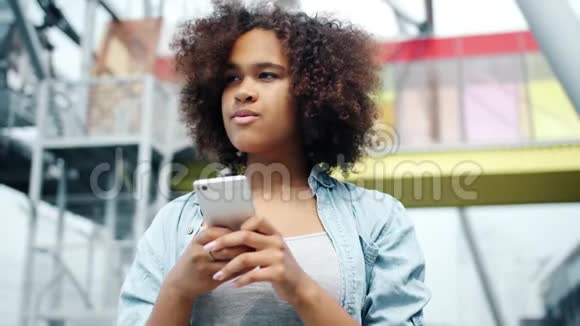 美国黑人女士笑着在城市户外看智能手机屏幕视频的预览图