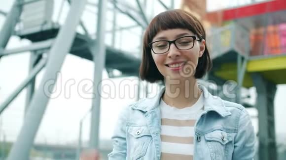 戴眼镜的女孩慢动作抚摸头发微笑着看着室外的摄像机视频的预览图
