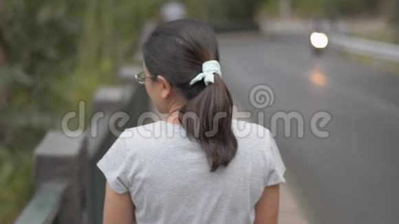 从亚洲女人的后侧看她戴着眼镜穿着休闲服装悠闲地走在沿路的小径上视频的预览图