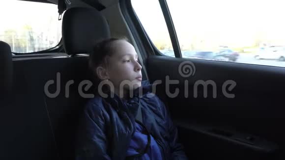 悲伤的小女孩坐在车里看着窗外的道路和周围的风景他的头在他身上视频的预览图