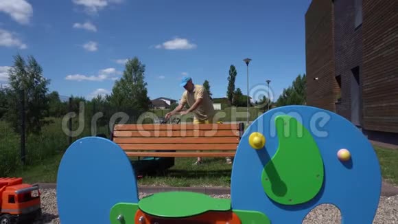 年轻人在孩子们五颜六色的操场附近割草万向节运动视频的预览图