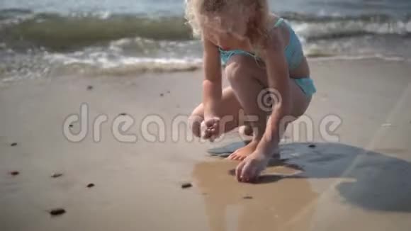 可爱的金发女孩在海边收集鹅卵石视频的预览图
