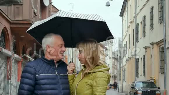 中年妇女和她年迈的丈夫一起在户外站在铺好的街道上撑着伞视频的预览图