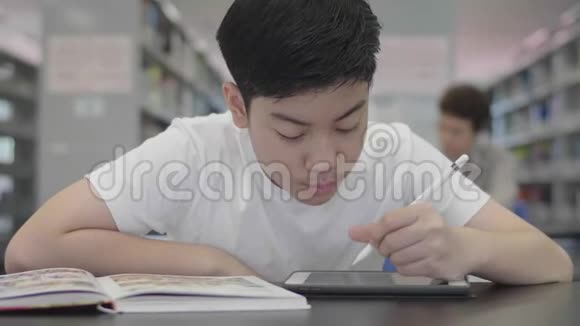 亚洲预科男孩使用平板电脑在图书馆两个男孩微笑着在平板电脑上画画视频的预览图