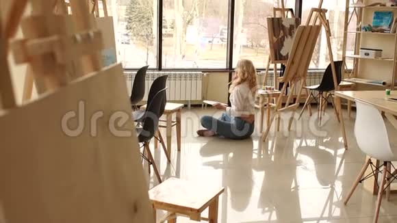 一个年轻的女孩有一个调色板和刷子坐在艺术工作室的地板上视频的预览图