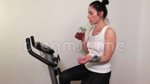 运动自行车上的女人喝冰沙检查血压视频的预览图
