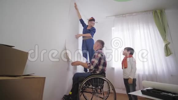 年轻幸福的家庭幸福的父亲坐轮椅的残疾人妻子和快乐的儿子正在选择新的壁纸视频的预览图