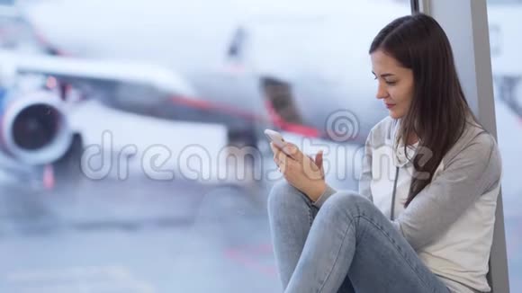 女人坐在机场用电话背景模糊的飞机视频的预览图