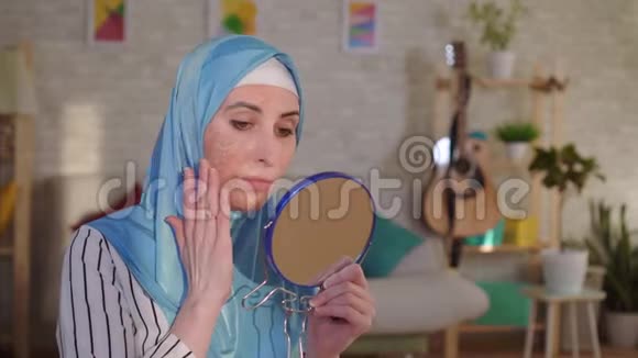戴着头巾的穆斯林妇女从镜子里看着她脸上烧伤的伤疤哭了起来视频的预览图