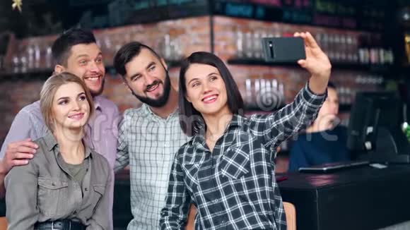 一群快乐的年轻朋友在酒吧的非正式会议上用智能手机自拍视频的预览图