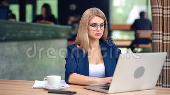时尚眼镜中的一位热情可爱的商业女性在咖啡馆里使用笔记本电脑视频的预览图