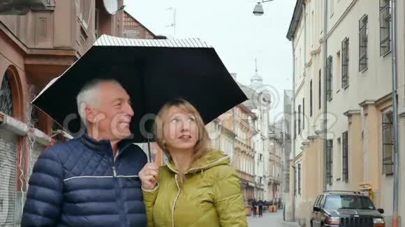 中年妇女和她年迈的丈夫一起在户外站在铺好的街道上撑着伞视频的预览图