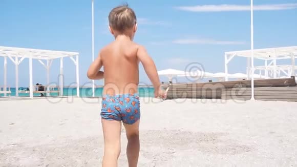 快乐的小男孩在海滩上沿着海滨跑步视频的预览图