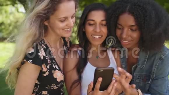 三位不同的女性朋友在公园里玩手机分享社交上的数字内容视频的预览图