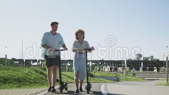 快乐的一对夫妇在夏天的公园里用电动滑板车散步视频的预览图