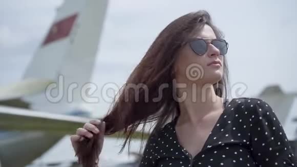 穿着太阳镜的年轻黑发女孩在飞机前摸着她的黑发旅行概念视频的预览图