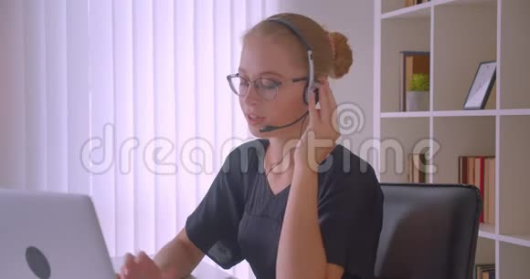 戴着眼镜和耳机的年轻白种人女商人用笔记本电脑打电话的特写照片视频的预览图