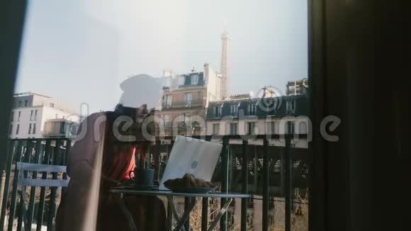 美丽的旅游妇女使用笔记本电脑坐在田园诗般的巴黎公寓阳台透过窗户玻璃反射视频的预览图