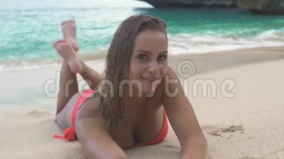 迷人的女人穿着比基尼躺在沙滩上微笑着拍摄蓝色的海洋景观美女模特视频的预览图