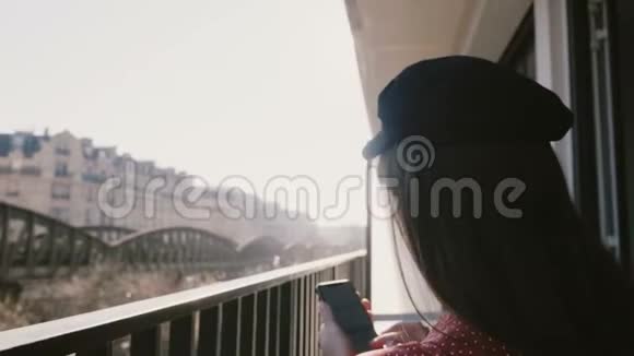 后景镜头耀斑特写幸福美丽优雅的女人使用智能手机在田园阳光明媚的早晨巴黎阳台视频的预览图