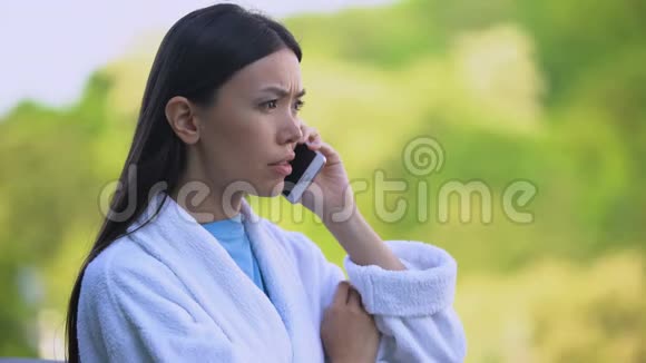 穿着浴袍的年轻女性在户外打电话时心烦意乱压力很大视频的预览图
