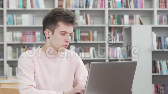一个年轻人在图书馆的笔记本电脑上工作看上去很体贴视频的预览图