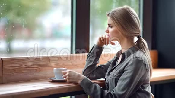 秋天雨天美丽忧郁的金发碧眼的不幸女子望着窗外坐在咖啡馆里视频的预览图
