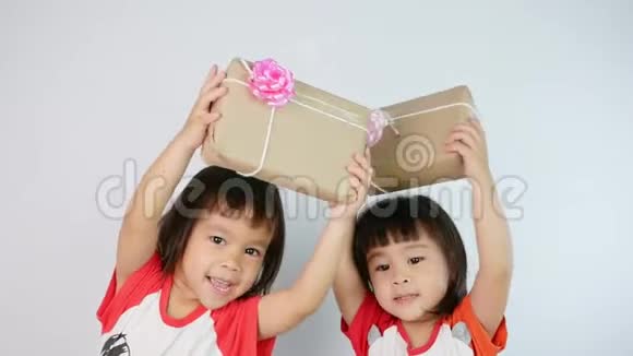 快乐的亚洲小女孩和她的妹妹拿着一个用回收纸包装的礼品盒孤立在白色背景上视频的预览图