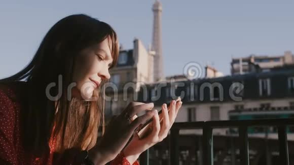 快乐美丽的旅游妇女使用智能手机社交网络应用程序在上午咖啡馆阳台与阳光埃菲尔铁塔景视频的预览图