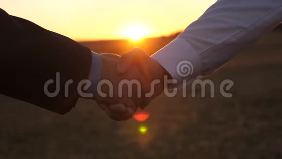日落时握手穿着蓝色衬衫和夹克的男人和穿着白色衬衫的男人在日落时分用美丽的光线握手视频的预览图