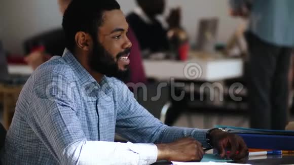 特写幸福微笑年轻英俊的黑人经理男子与同事在时尚阁楼多民族办公桌交谈视频的预览图