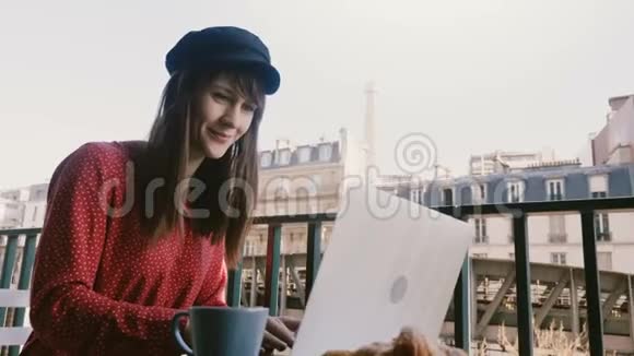 微笑着快乐优雅的女商人使用笔记本电脑在田园诗般的巴黎早阳台上看着埃菲尔铁塔的早餐视频的预览图