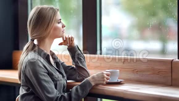 忧郁的年轻女子注视着窗外潮湿的雨天坐在咖啡馆里视频的预览图