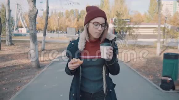 女孩在公园里散步慢慢地喝咖啡穿着夹克和帽子的女孩视频的预览图