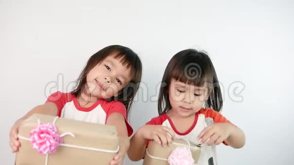 快乐的亚洲小女孩和她的妹妹拿着一个用回收纸包装的礼品盒孤立在白色背景上视频的预览图