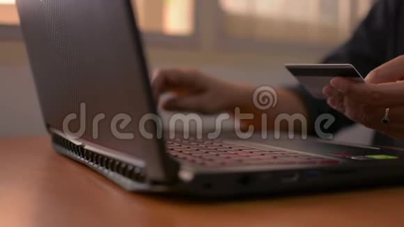 一个女人的手拿着一张信用卡在桌子上键入笔记本电脑键盘进行在线支付视频的预览图