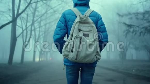 年轻运动女性的后景穿着蓝色羽绒服带引擎盖和小城市背包视频的预览图