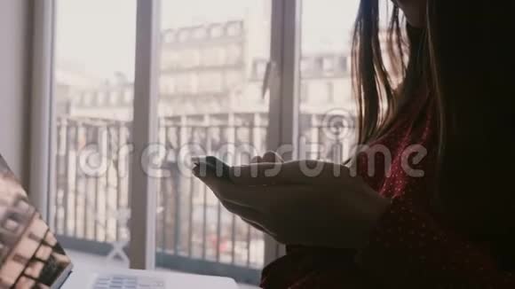 成功的年轻快乐女商人使用智能手机和笔记本电脑在巴黎公寓窗口度假特写视频的预览图