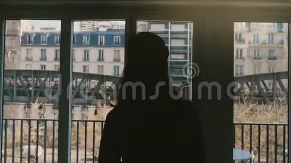 镜头跟随年轻幸福的女人剪影走着打开阳台的窗户欣赏阳光明媚的埃菲尔铁塔景观慢动作视频的预览图