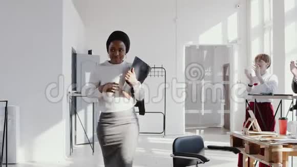 快乐微笑的年轻非洲女经理带着一个盒子进入新的办公室受到同事慢动作红色EPIC的欢迎视频的预览图