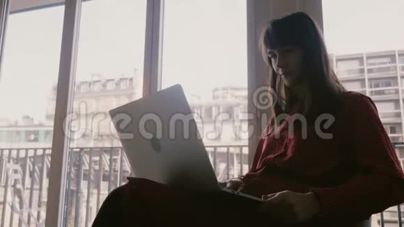 快乐美丽的年轻女商人微笑着使用笔记本电脑在巴黎的公寓窗口火车经过视频的预览图