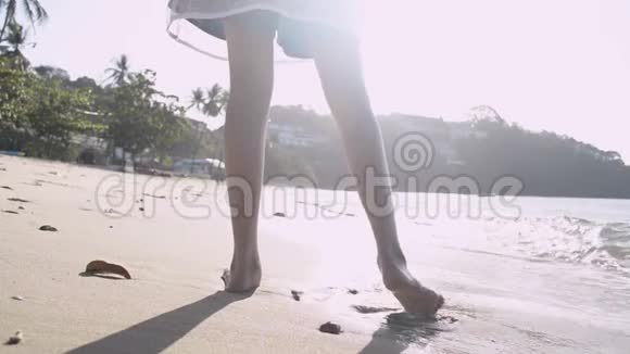 从亚洲女孩背着草帽穿着休闲服装光着脚在阳光下的海滩上行走视频的预览图